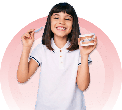 A smiling young girl holding a clear dental aligner in one hand and a teeth model with braces in the other.